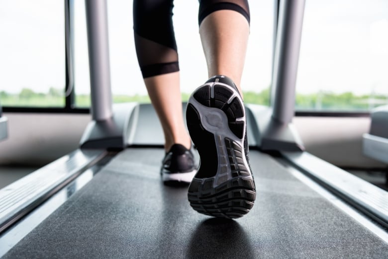 A close up view of a treadmill from behind, showing the lower half of a person's legs and their sneakers.