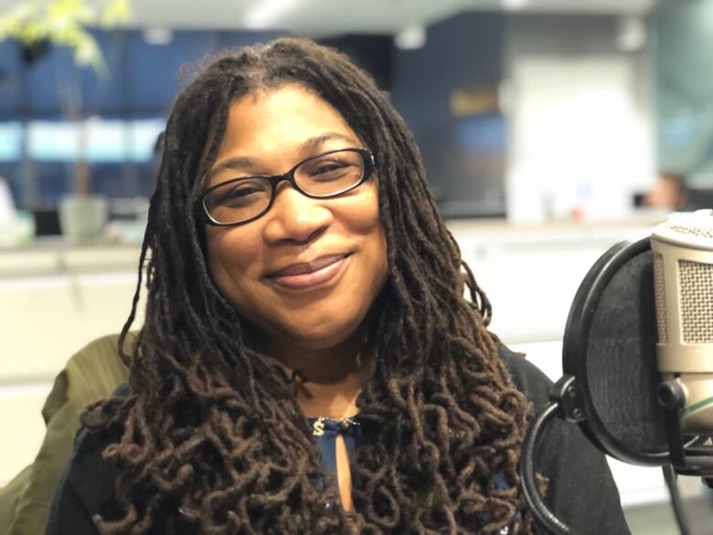 A Black woman smiles as she sits behind a microphone in a radio studio.