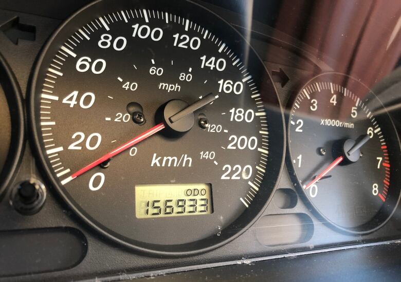 A car odometre is shown reading 156,933 kilometres.