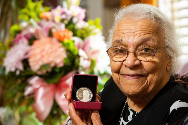 An older Black woman with white hair holding a coin