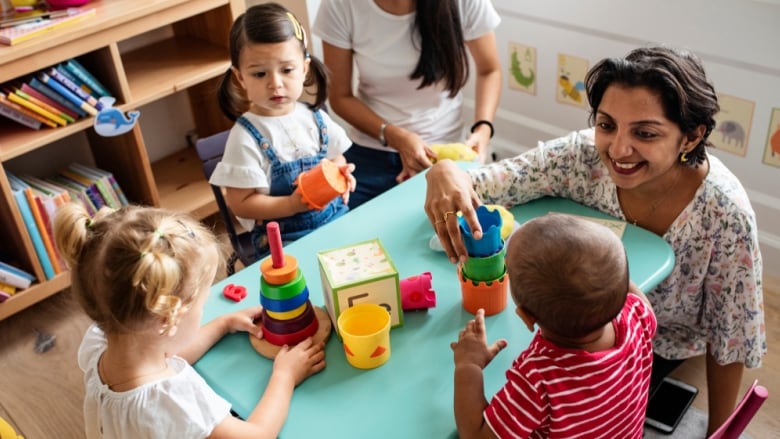 Children and a daycare worker sitting around a blue table.