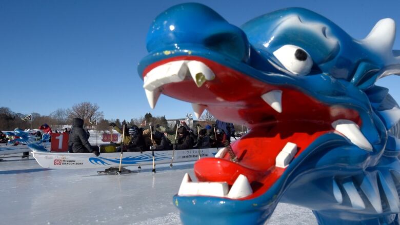 A blue dragon on the front of a boat about to race on an icy canal.