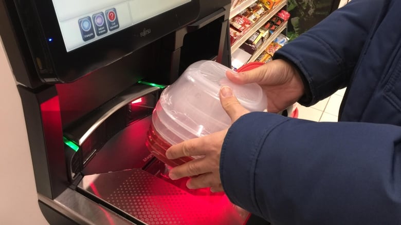 A person scans a set of plastic containters at self-checkout. 