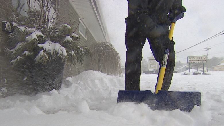 A person, seen from the waist down, shovelling snow.