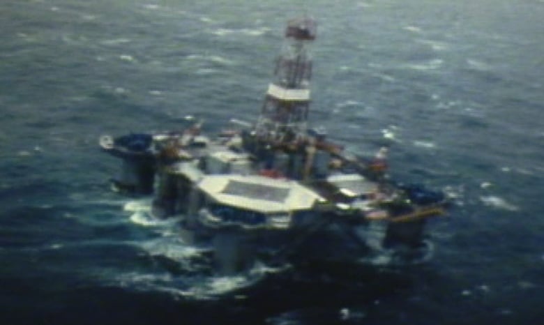 An oil drilling rig floats in the middle of blue ocean waters.