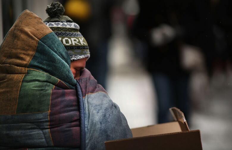 A person wrapped up in a blanket outside, with a toque on.