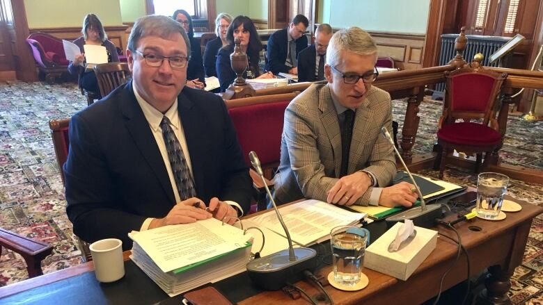 Two men sitting at a desk with open binders in front of them