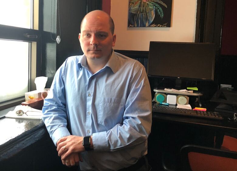 A man with a blue shirt stands in an office. 