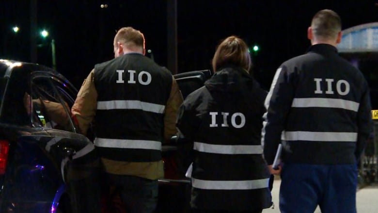 Three officers with the lettering IIO on the back of their uniforms are pictured together at a crime scene.