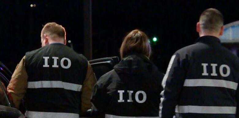 Three officers with the lettering IIO on the back of their uniforms are pictured together at a crime scene.