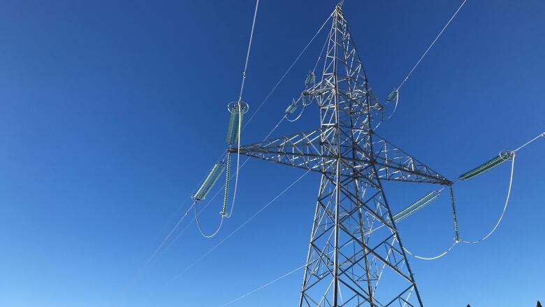 A steel electrical tower in the middle of a snowy field on a clear day.