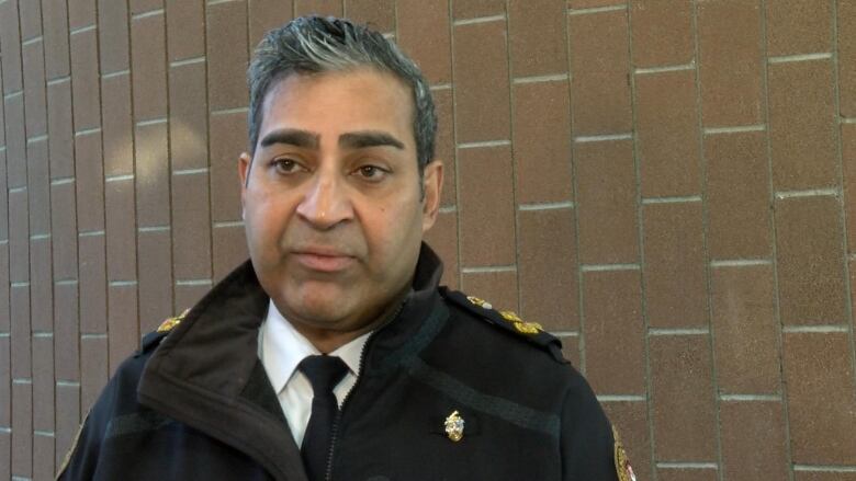 A middle-aged south Asian man wearing a shirt and tie, and a police jacket. 