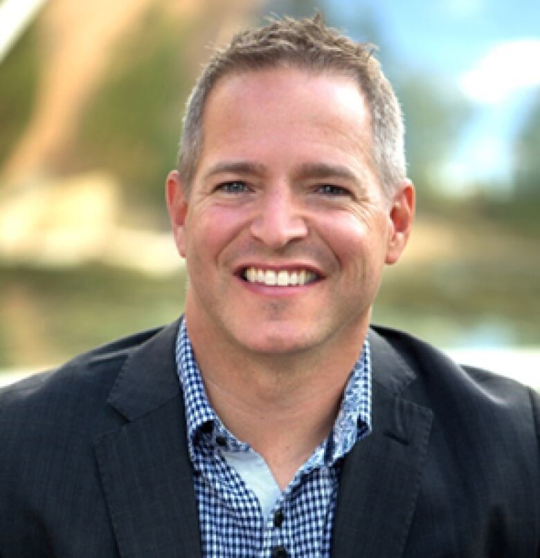 Smiling man with short greyish hair wearing a blazer with a blurred background 