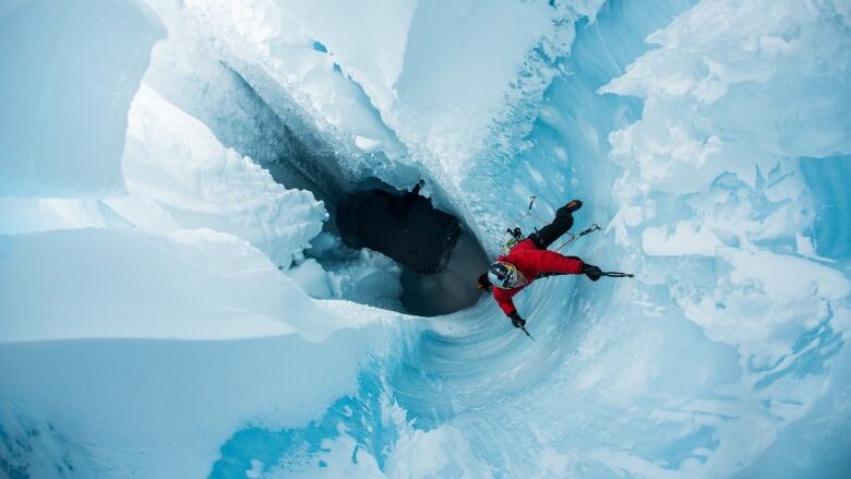 Ice climber Will Gadd in red shown from above rappelling into a blue hole which is Greenland's ice cap.