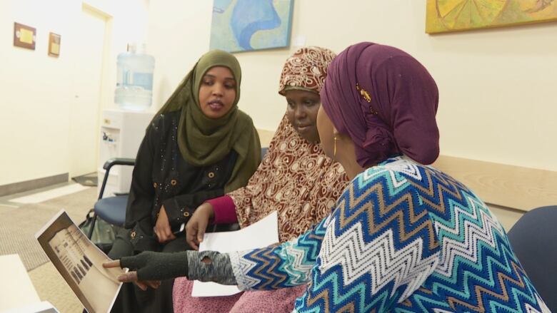 Women from Somalia consult with another woman showing them something on a computer.