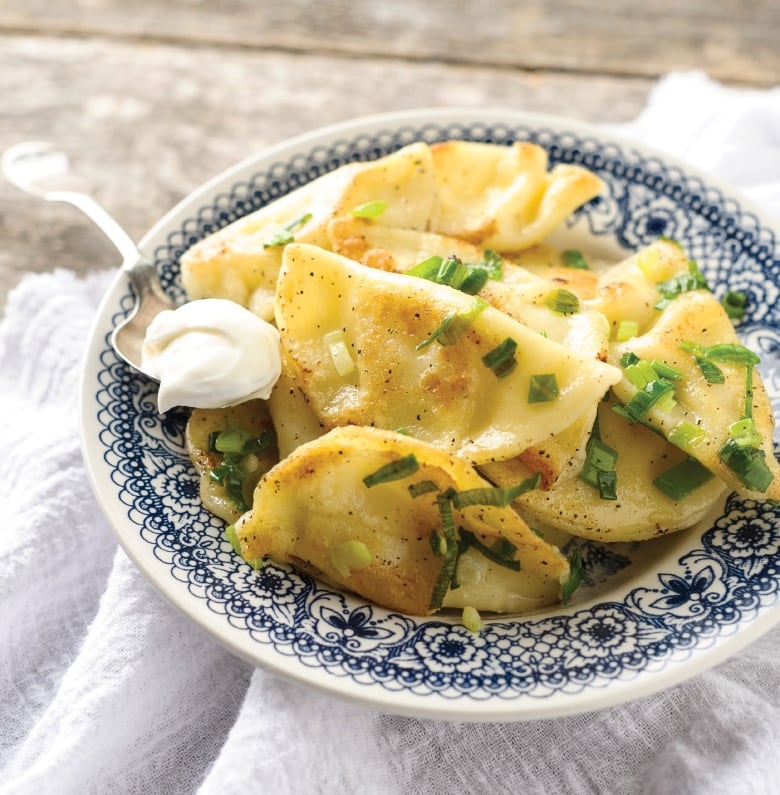 Closeup on a plate of perogies with a spoon with sour cream resting on the side. 