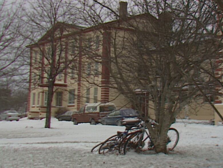 An old photo of a three-storey brick building behind trees and snow-covered grass.