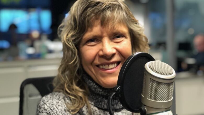 A woman with blonde hair, smiling and sitting behind a microphone. 