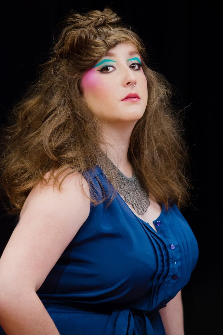 A woman, wearing colourful eye make up, stares into the camera. 