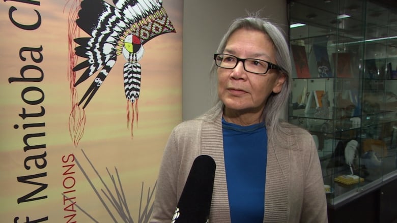 A woman wearing a blue shirt stands near an Assembly of Manitoba Chiefs sign. 