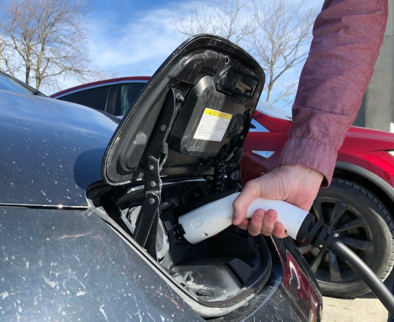 A hand plugs a charger into an electric vehicle.