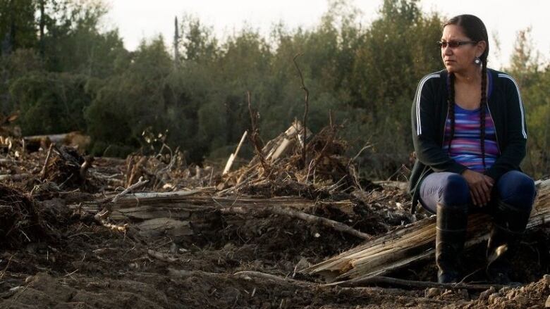 a woman sits on broken wood from a fallen tree