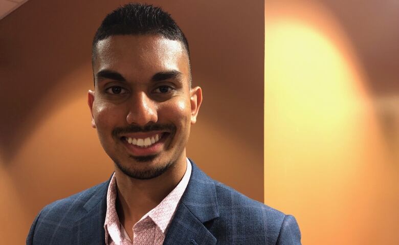 A smiling man in a suit looks at the camera.