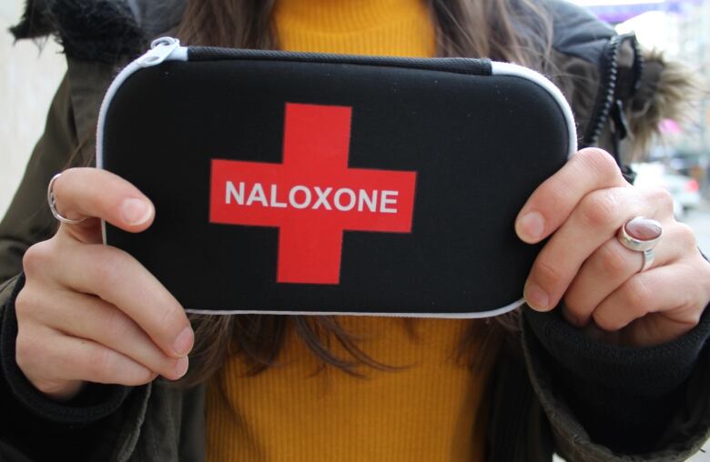 A person holds a black pouch that reads naloxone. 