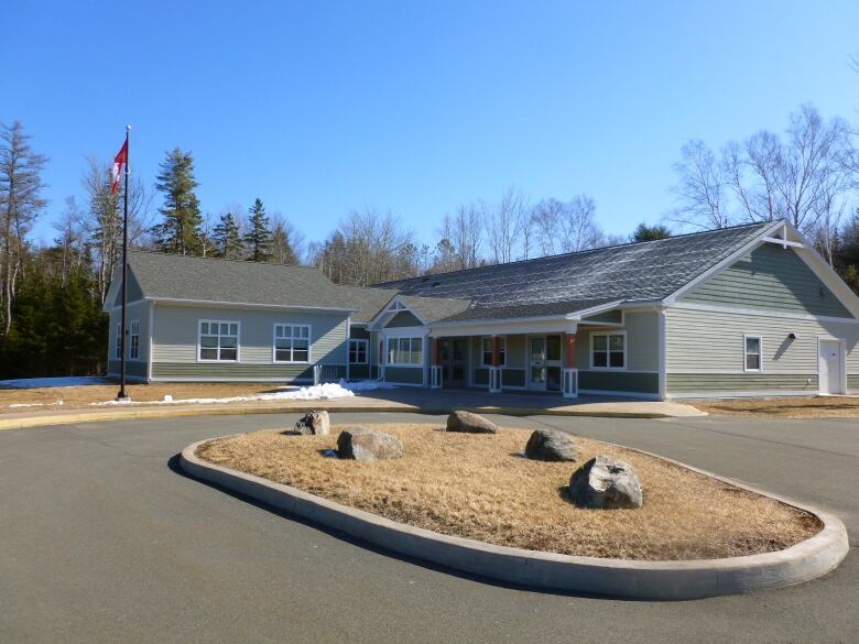 A one-story beige building is seen with a Canadian flag flying on the pole outside.