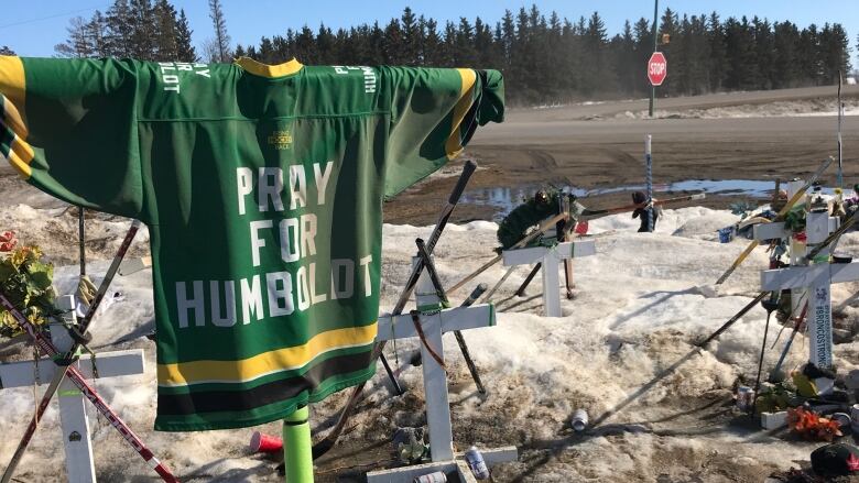 A 'pray for Humboldt' jersey is draped at the site that also fetures crosses, hockey sticks and other tributes.