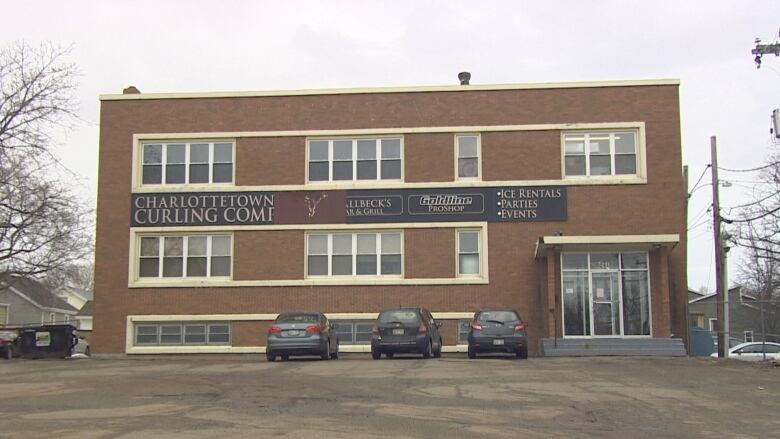 A large brick building with a sign that says Charlottetown Curling Club. Three cars are parked in front of it. 