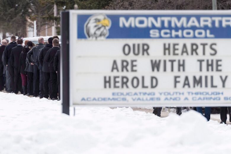 A billboard reads 'Our hearts are with the Herold family.