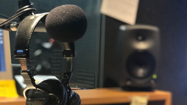 A headset is pictured hung up over a microphone in a radio booth. 