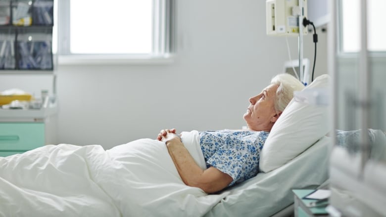 A woman with white hair in a hospital bed staring up.