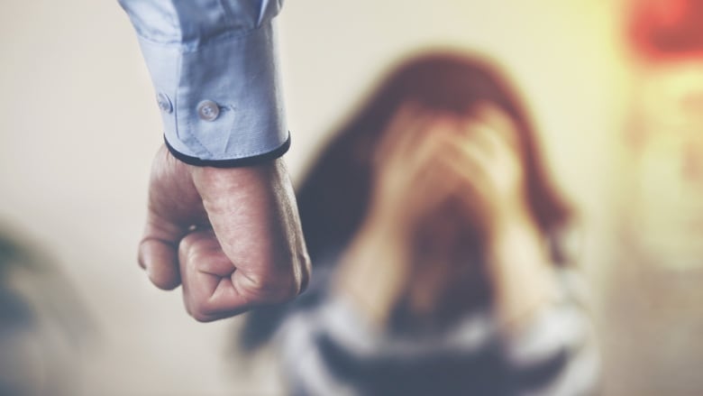 A blurred photo shows a closeup of a man's fist with a woman holding her head in her hands in the background.