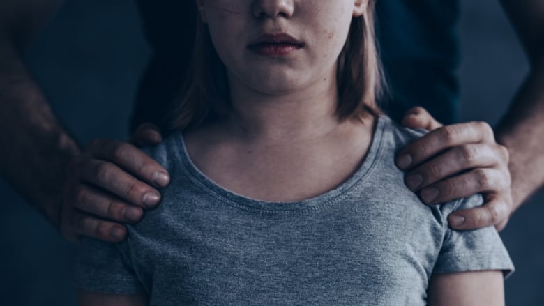 Two adult hands hold the shoulders of an unidentified pre-teen girl. 