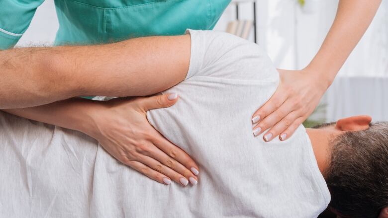 A person with two hands on the back of someone lying down in a medical gown.