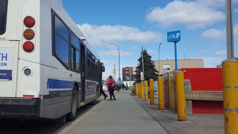 Photograph taken from behind a bus, that people are boarding in the summer.