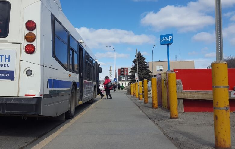 Photograph taken from behind a bus, that people are boarding in the summer.