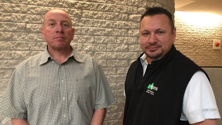 Two men stand in front of a wall in a courthouse.