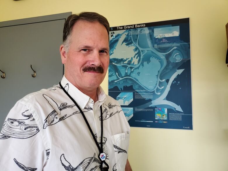 A man wearing a white shirt standing in front of a map. 