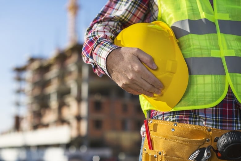 A close up of a man in a construction vest holding a safety helmet.