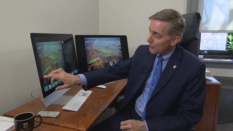 A man in a suit gestures to a computer screen.