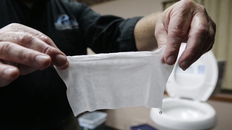 A person holds up a flushable wipe in front of a toilet