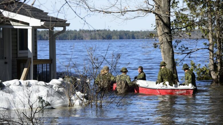 Soldiers in the flooded waters walking with a boat.