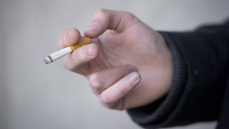 A person's hand holding a cigarette is pictured.