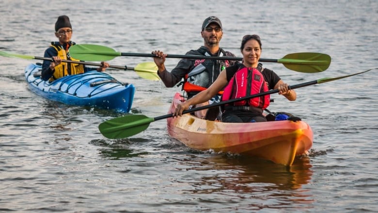 A family is pictured paddling on two kayaks, an orange one and a blue one.