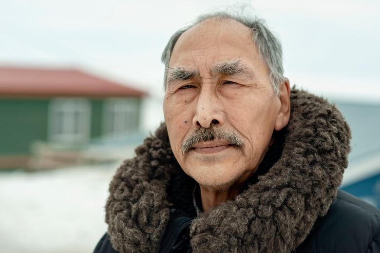 A man wearing a parka is seen in a close up looking at the camera. 