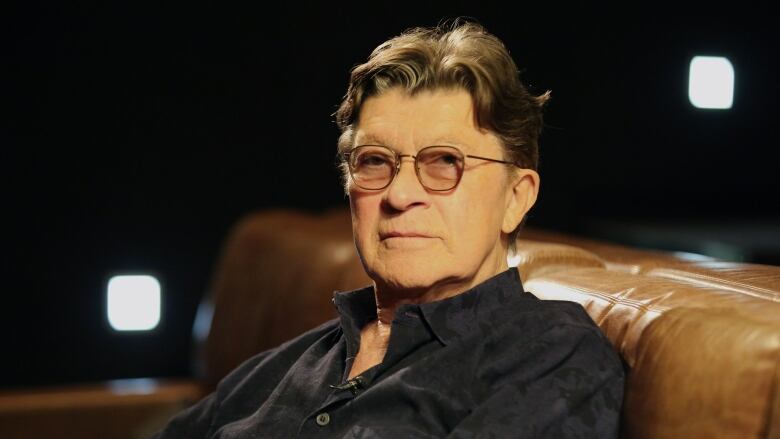 A man wearing glasses sits in a dimly lit theatre.