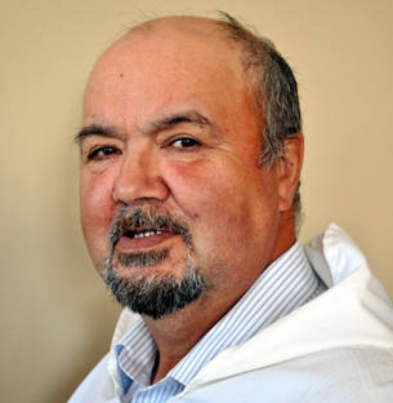 A man is wearing a white coat and blue striped button up. 